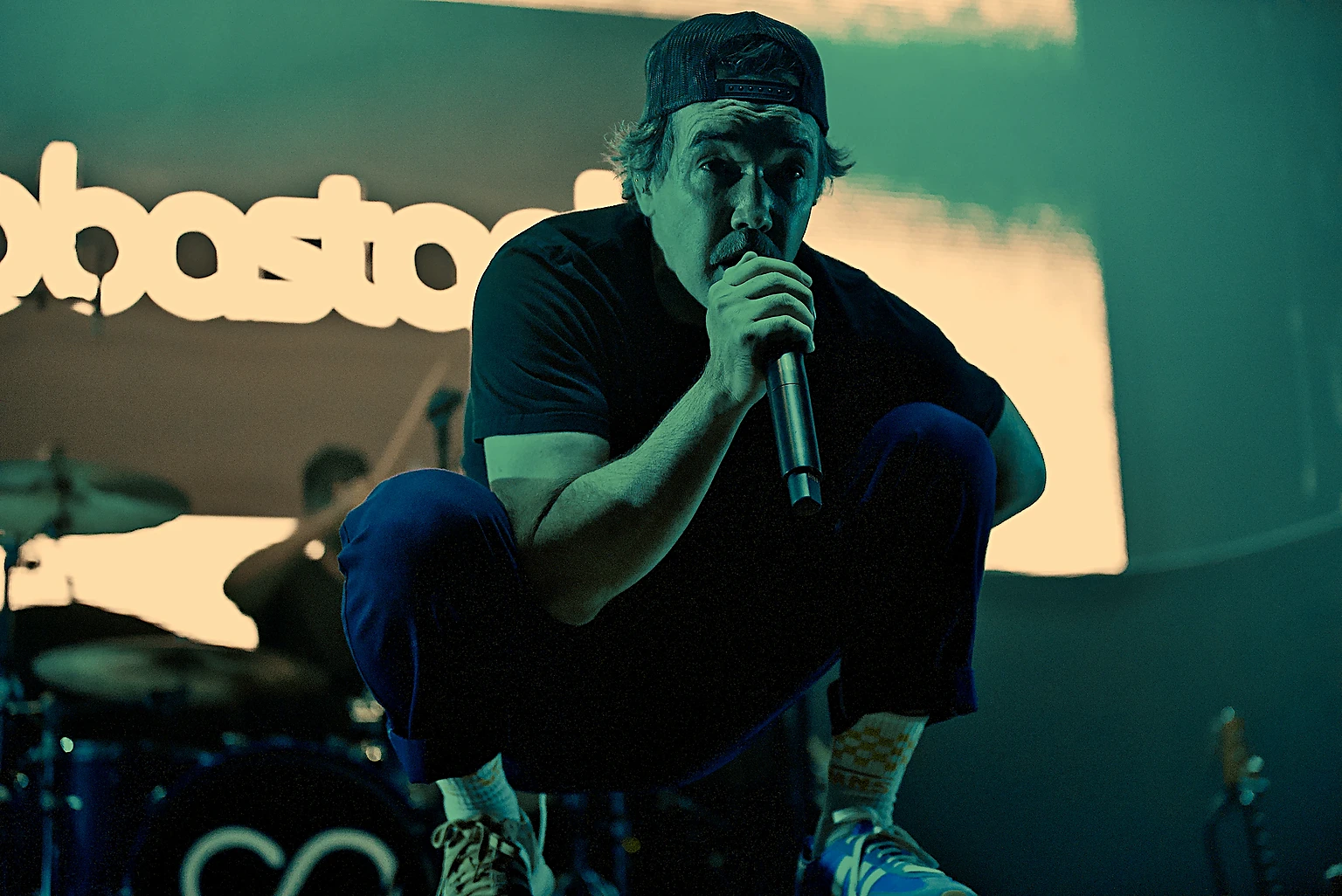 Hoobastank vocalist Doug Robb crouched and singing in front of the Hoobastank backdrop at Toyota Arena, Ontario