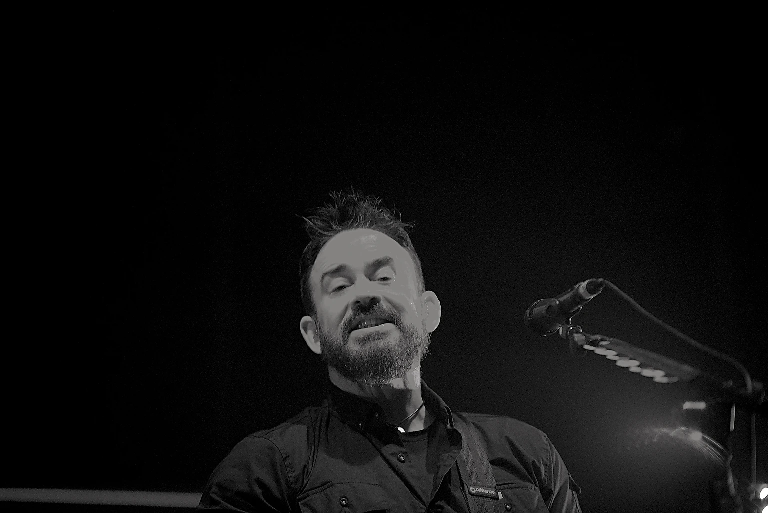 Black and white photo of a Seether musician smiling at the microphone at Toyota Arena, Ontario